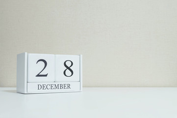 Closeup white wooden calendar with black 28 december word on blurred white wood desk and cream color wallpaper in room textured background with copy space , selective focus at the calendar