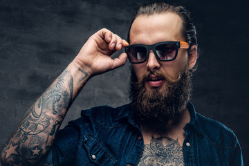 Obraz premium Tattooed bearded man touches sunglasses on his face.