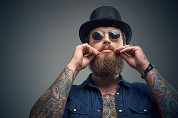 Tattooed bearded male in sunglasses and top hat.