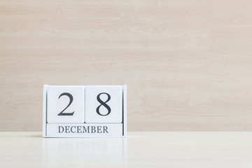 Closeup surface white wooden calendar with black 28 december word on blurred brown wood desk and wood wall textured background with copy space , selective focus at the calendar