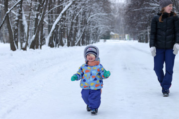 Fototapeta na wymiar Child goes with mother on a snowy road in winter Park