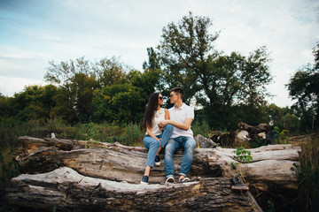 Couple love. Beautiful couple in summer denim clothes and sunglasses sitting on stump and smiling each other. Couple in love.