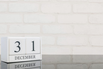 Closeup white wooden calendar with black 31 december word on black glass table and white brick wall textured background with copy space , selective focus at the calendar