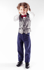 Cute curly boy in a silver waistcoat is facing the camera with his eyes closed and ears and mouth open. Full length. Gray background.
