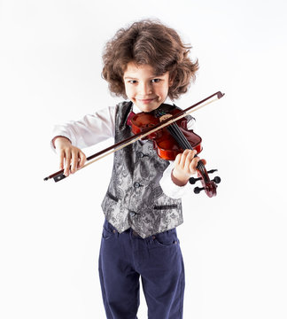 Cute cheerful curly-haired boy in a waistcoat playing the violin. Close-up. Gray background.