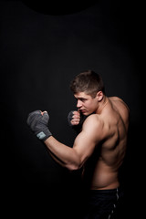 Fototapeta na wymiar Muscular athletic man boxing on a black background. A man with a naked torso in shorts, hands peremotanye bandages for boxing.