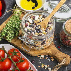 Assorted legumes grains on a light background with ripe tomatoes, olive oil, herbs, pepper ingredients for lunch or dinner. Top view. The concept of  healthy home-cooked meal.