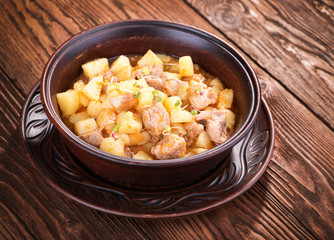 Stew with potatoes and meat in a ceramic plate on a wooden table