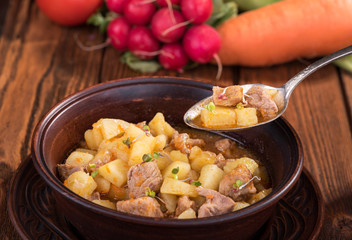 Stew with potatoes and meat in a ceramic plate on a wooden table