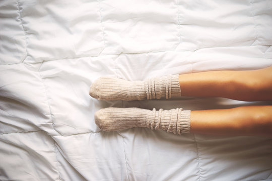 Warm and cozy white socks in the bed, top view