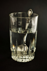 Vaso de agua con cuchara sobre fondo negro