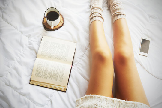 Soft photo of woman on the bed with book and cup of coffee, top view