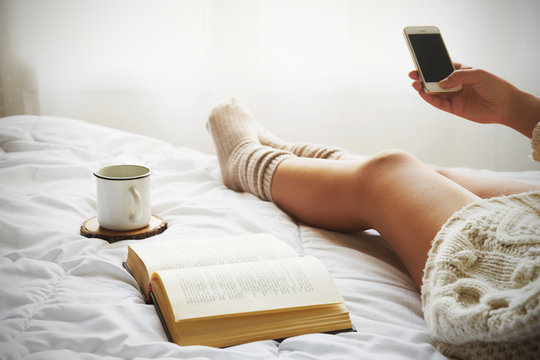 Soft photo of woman on the bed with old book, a cup of coffee and smart phone