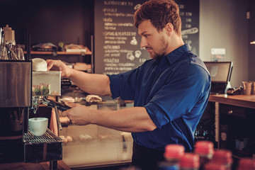 Handsome barista preparing cup of coffee for customer in coffee shop