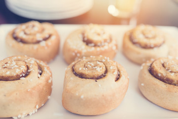 Cinnamon rolls on white plate. Sun and vintage effect applied.