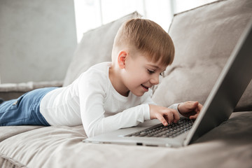 Joyful boy using laptop computer while lies on sofa