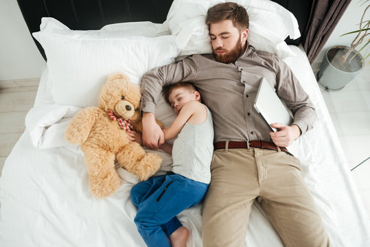 Little boy sleeping at home in bed with bearded father