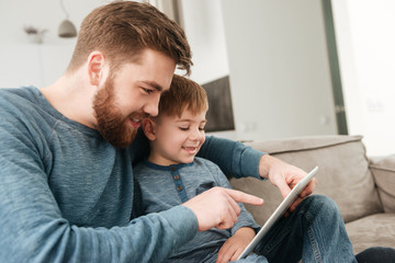 Handsome father using tablet computer with his little cute son.