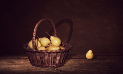 Pears in a wicker basket on dark painting background.
