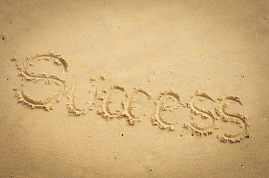 Success words hand writing on sand beach texture background.
