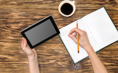 Woman looking on the tablet PC and writing information to notebo