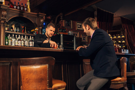 Smiling attractive young barman wiping glasses and talking to man in bar