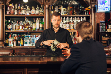 Smiling attractive young barman wiping glasses and talking to man in bar