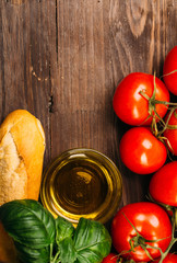 Italian food background with vine tomatoes, basil, olive oil ingredients and baguette on dark wooden rustic table Copy space Top view