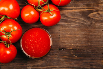 Bowl of ketchup or tomato sauce and fresh tomatoes on dark wooden background
