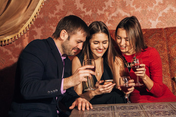 two cute women and a man sitting in  restaurant  use the phone