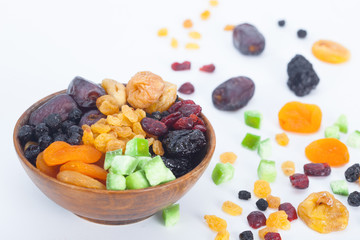 Mix of dried fruits in wooden bowl, white background.