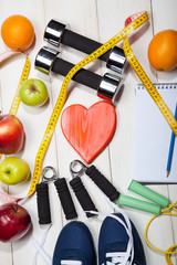 Heart, dumbbells and fruits, apples, oranges on a white wooden background