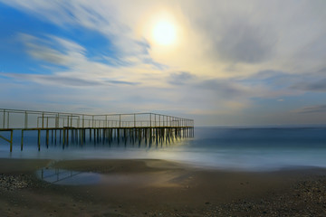 night view of the sea, the full moon illuminates the beach and pier. Slow shutter speed
