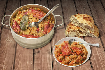 Cabbage with Smoked Ribs in Stainless Steel Saucepot and Porcelain White Plate with Pitta Bread Served on Rustic Pine Wood Table