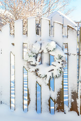 Snow covered Christmas wreath covered in snow on a garden fence.