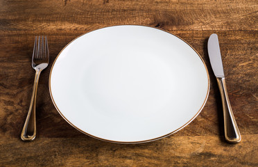 Empty luxurious white plate with knife and fork on wooden table, high angle view