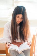 Woman sitting on wood chair holding book to read in library