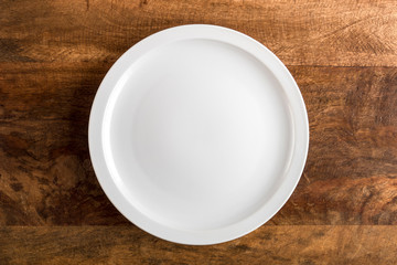 Empty white plate on wooden table, top view