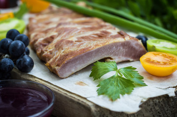 Smoked pork ribs with grape sauce, herbs and vegetables. Wooden background. Top view. Close-up