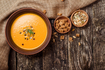 Bowl of pumpkin soup with bread crouton on dark wooden table.