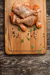 Raw chicken drumstick on wooden board with salt, garlic, rosemary, spices.