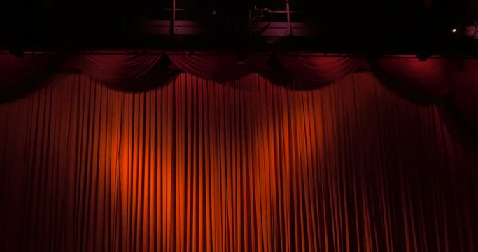 A closed red stage curtain in a theater