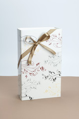 Gift box with golden ribbon bow on light brown and white background.