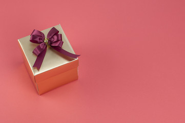 Gold gift box with ribbon bow on light red background.