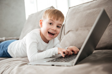 Happy boy using laptop computer while lies on sofa