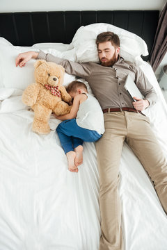Boy sleeping in bed with his bearded father and toy.