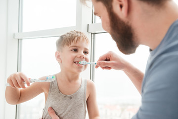 Happy father and son smiling while brushing teeth in bathroom.