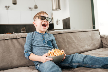 Little boy sitting on sofa watching TV with 3d glasses