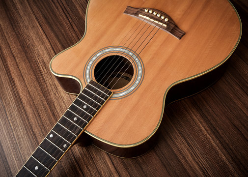 Acoustic guitar laid on wooden floor background.
