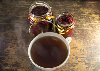 Two jars cherry jam and a Cup of tea on a wooden table. Wooden background